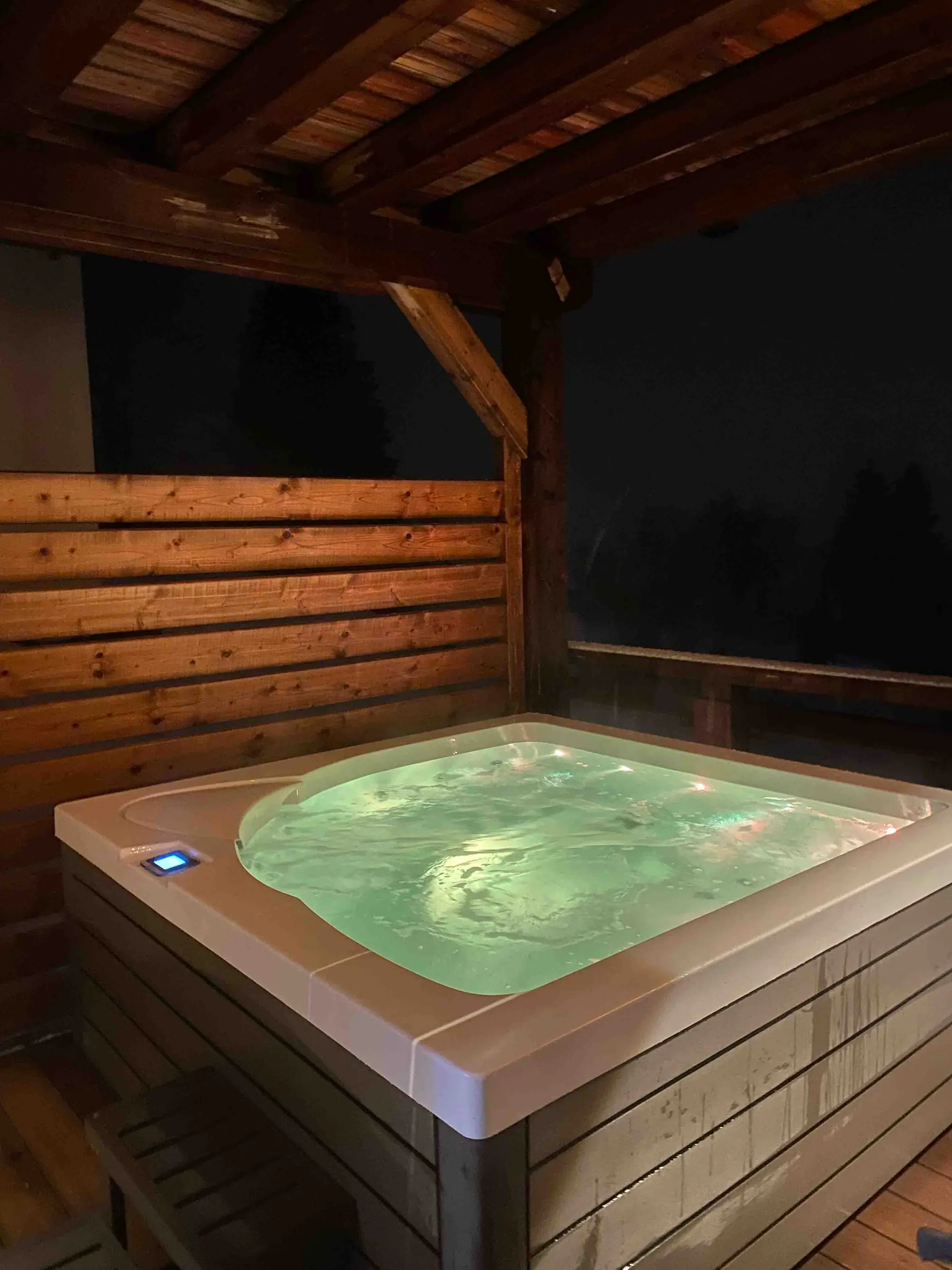 The chalet's outdoor hot tub lit up at night on the terrace
